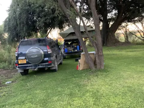 An SUV with a rooftop tent set up at a shaded campsite